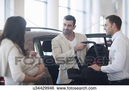 Mid adult couple with baby girl chatting about baby seat in car dealership View Large Photo Image Stock Photograph - Mid adult couple with baby girl chatting about baby seat in car dealership. Fotosearch