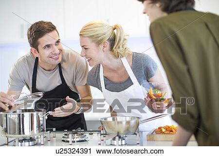 Stock Image - Mid adult man and friends preparing food in kitchen. Fotosearch