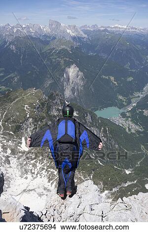 Picture - Mid adult man BASE jumping from mountain edge, Alleghe, Dolomites, Italy. Fotosearch