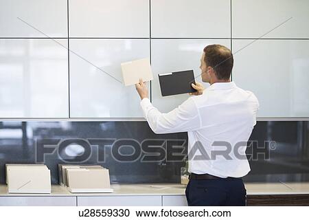 Stock Image - Mid adult man holding up ceramic tiles in kitchen showroom. Fotosearch