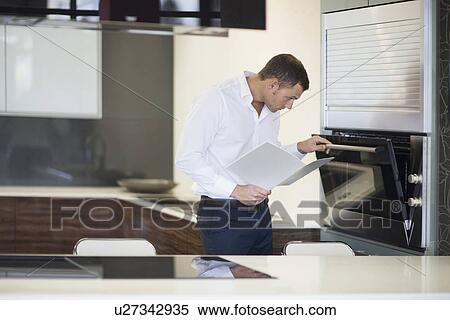 Stock Photography - Mid adult man inspecting oven in kitchen showroom. Fotosearch
