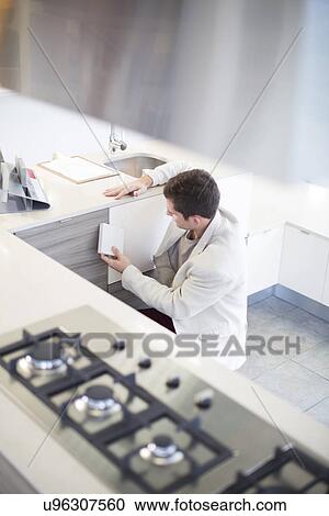 Stock Image - Mid adult man looking at ceramic tiles in kitchen showroom. Fotosearch