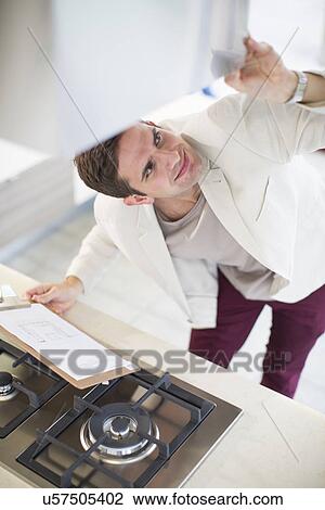 Stock Image - Mid adult man looking at extractor hood in kitchen showroom. Fotosearch