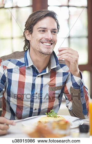 Stock Photograph - Mid adult man sitting at restaurant table. Fotosearch
