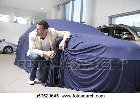 Mid adult man uncovering and peeking at new car in car dealership View Large Photo Image Stock Photography - Mid adult man uncovering and peeking at new car in car dealership. Fotosearch