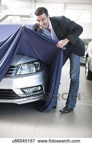Mid adult man uncovering new car in car dealership View Large Photo Image Stock Photo - Mid adult man uncovering new car in car dealership. Fotosearch