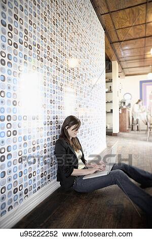 Stock Image - Mid adult woman sitting on floor using laptop. Fotosearch