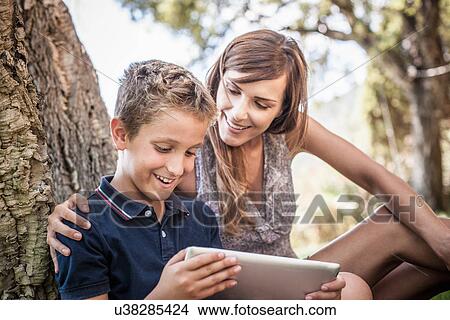 Mother and son looking at digital tablet in holiday home garden, Capoterra, Sardinia, Italy View Large Photo Image Picture - Mother and son looking at digital tablet in holiday home garden, Capoterra, Sardinia, Italy. Fotosearch