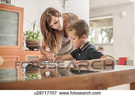 Mother and son looking down at homework at dining room table View Large Photo Image Stock Photo - Mother and son looking down at homework at dining room table. Fotosearch