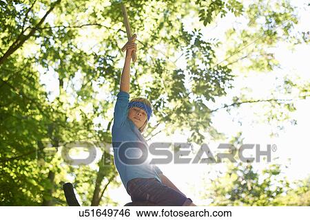 Stock Photograph - One young boy with toy sword, sitting on tree branch. Fotosearch