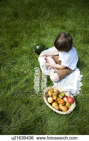 Stock Photograph - Overhead view of boy cross legged on grass pouring milk into glasses. Fotosearch