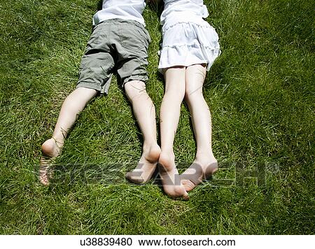 Stock Image - Overhead view of brother and sisters legs as they lay on grass. Fotosearch