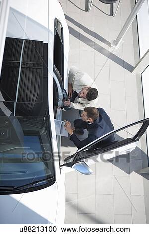 Stock Image - Overhead view of salesman and customer inspecting new car in car dealership. Fotosearch