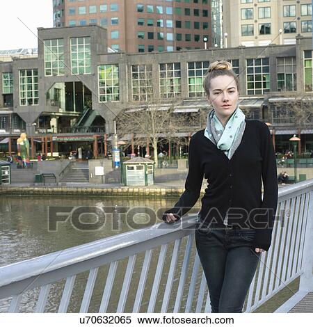 Stock Photography - Portrait of confident young woman on river bridge in city. Fotosearch