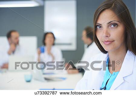 Stock Photo - Portrait of female doctor, colleagues having discussion behind. Fotosearch