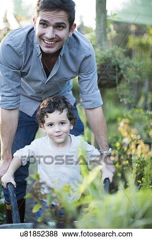 Portrait of mid adult man and son pushing wheelbarrow in allotment View Large Photo Image Stock Photo - Portrait of mid adult man and son pushing wheelbarrow in allotment. Fotosearch
