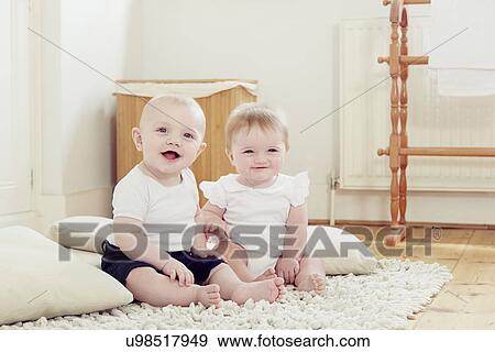 Stock Photo - Portrait of smiling baby girl and baby boy sitting on rug. Fotosearch