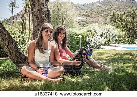 Portrait of two female friends with dog in holiday home garden, Capoterra, Sardinia, Italy View Large Photo Image Stock Photo - Portrait of two female friends with dog in holiday home garden, Capoterra, Sardinia, Italy. Fotosearch