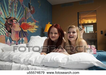 Stock Photo - Portrait of two young women lying on hotel bed. Fotosearch