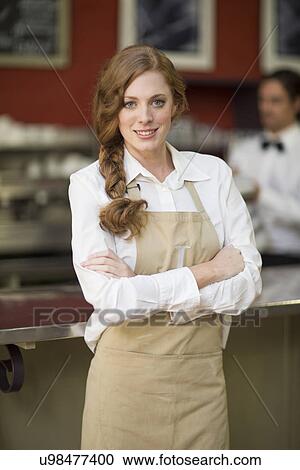 Stock Image - Portrait of waitress with arms folded in restaurant. Fotosearch