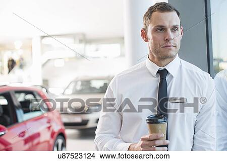 Picture - Portrait of worried salesman with takeaway coffee in car dealership. Fotosearch