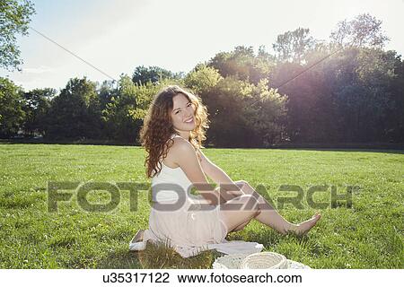 Stock Image - Portrait of young woman sitting on park grass. Fotosearch
