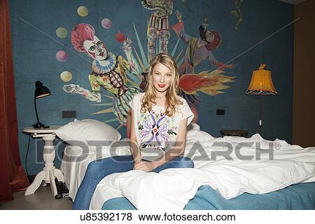 Stock Photo - Portrait of young woman sitting on hotel bed. Fotosearch
