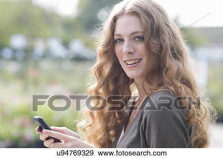Stock Photo - Portrait of young woman texting on smartphone in garden. Fotosearch