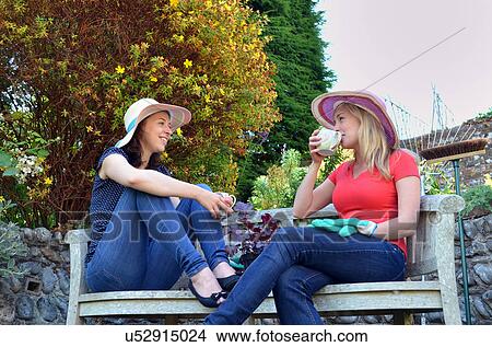 Picture - Portrait of young women sitting on bench drinking tea. Fotosearch
