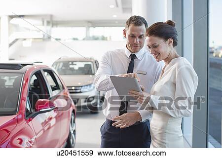 Salesman and female customer using digital tablet in car dealership View Large Photo Image Stock Photo - Salesman and female customer using digital tablet in car dealership. Fotosearch