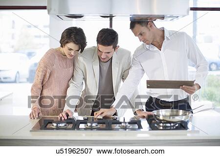 Stock Photo - Salesman and mid adult couple looking at hob in kitchen showroom. Fotosearch