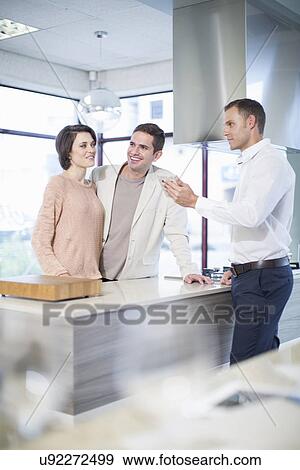 Stock Photo - Salesman and mid adult couple looking at ceramic tile in kitchen showroom. Fotosearch