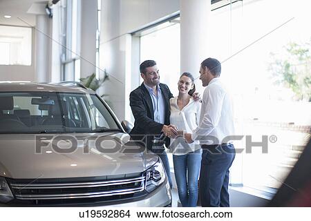 Salesman shaking hands with mid adult couple in car dealership View Large Photo Image Picture - Salesman shaking hands with mid adult couple in car dealership. Fotosearch