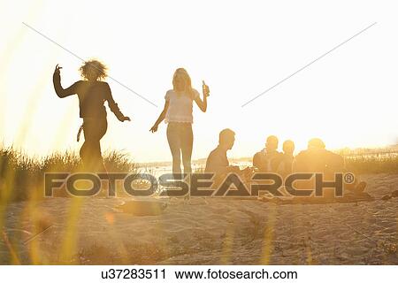 Stock Image - Six adult friends partying at sunset on Bournemouth beach, Dorset, UK. Fotosearch