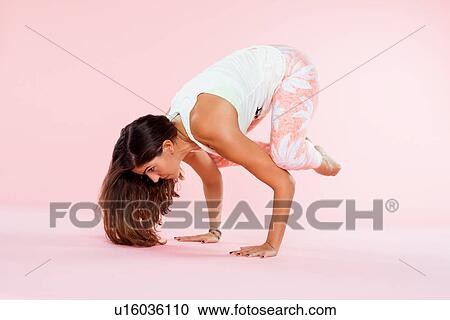 Stock Image - Studio shot of young woman in yoga position balancing with hands on floor and knees on elbows. Fotosearch