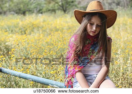 Sullen girl in cowboy hat sitting on fence gazing down View Large Photo Image Stock Photograph - Sullen girl in cowboy hat sitting on fence gazing down. Fotosearch