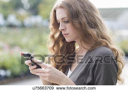 Sullen young woman reading texts on smartphone in garden View Large Photo Image Stock Photo - Sullen young woman reading texts on smartphone in garden. Fotosearch