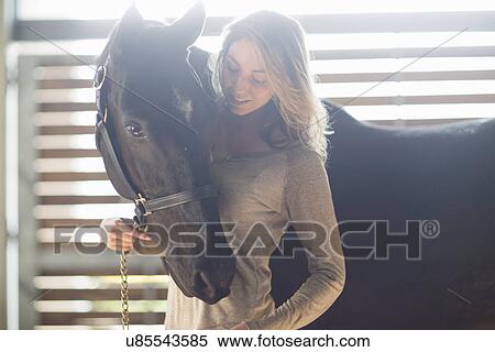 Stock Photography - Tender portrait of young woman with black horse. Fotosearch