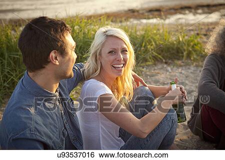 Stock Photograph - Three adult friends drinking beer on Bournemouth beach, Dorset, UK. Fotosearch