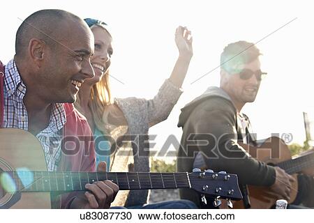 Stock Image - Three adult friends playing acoustic guitars on Bournemouth beach, Dorset, UK. Fotosearch