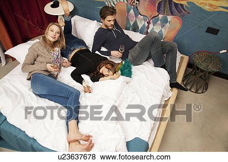 Three male and female adult friends lying on hotel bed drinking champagne View Large Photo Image Stock Photo - Three male and female adult friends lying on hotel bed drinking champagne. Fotosearch