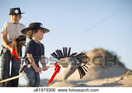 Stock Photograph - Two brothers dressed as cowboys with hobby horses in sand dunes. Fotosearch