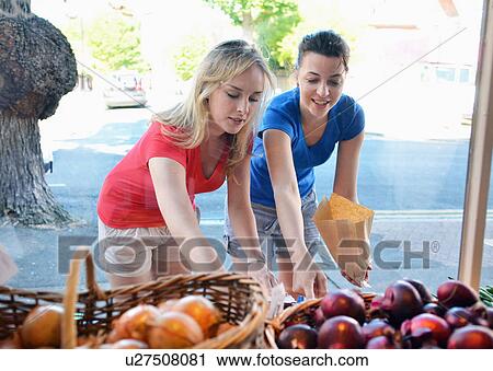 Two young women choosing food at market stall View Large Photo Image Stock Image - Two young women choosing food at market stall. Fotosearch