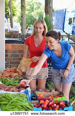 Two young women choosing fruit at market stall View Large Photo Image Stock Image - Two young women choosing fruit at market stall. Fotosearch