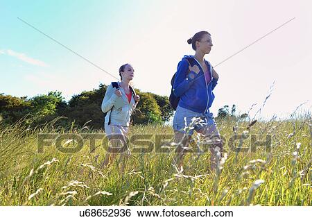 Two young women hiking through field View Large Photo Image Stock Photograph - Two young women hiking through field. Fotosearch