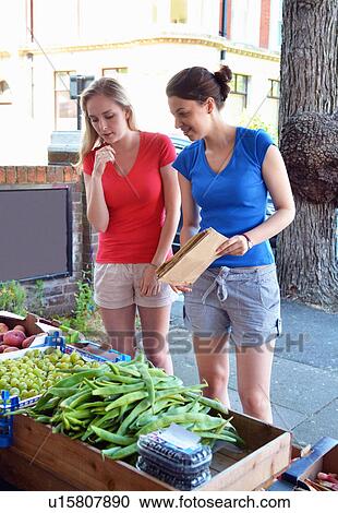 Two young women looking at vegetables at market stall View Large Photo Image Stock Image - Two young women looking at vegetables at market stall. Fotosearch