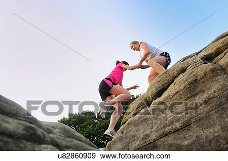 Two young women runners helping each other on top of rock formation View Large Photo Image Stock Photo - Two young women runners helping each other on top of rock formation. Fotosearch