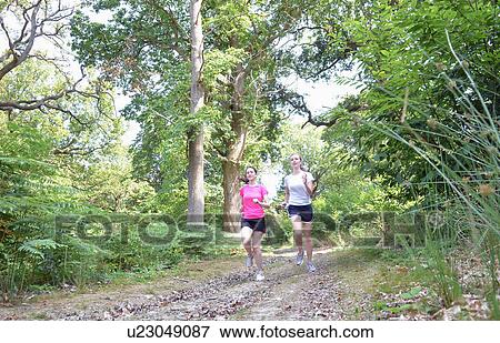 Stock Photo - Two young women runners running through forest track. Fotosearch