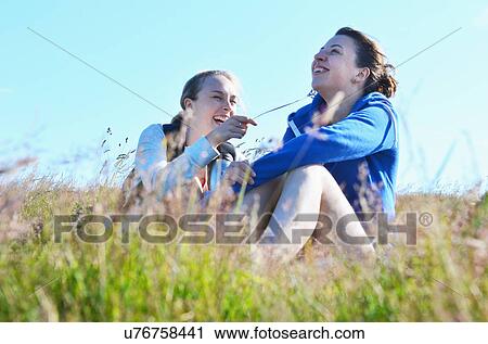 Stock Image - Two young women sitting field, one tickling the other. Fotosearch