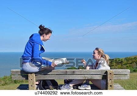 Two young women sitting on bench with map View Large Photo Image Stock Image - Two young women sitting on bench with map. Fotosearch
